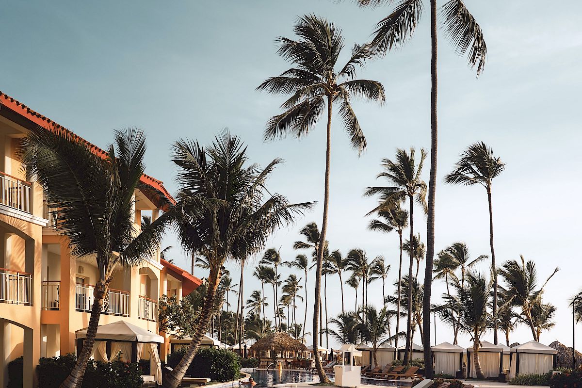 A serene poolside scene at a resort, featuring lounge chairs and tall palm trees against a clear sky, creating a relaxing atmosphere.